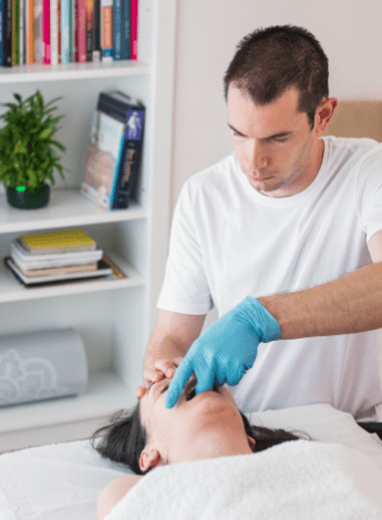 A physiotherapist performs jaw manipulation on a female patient 